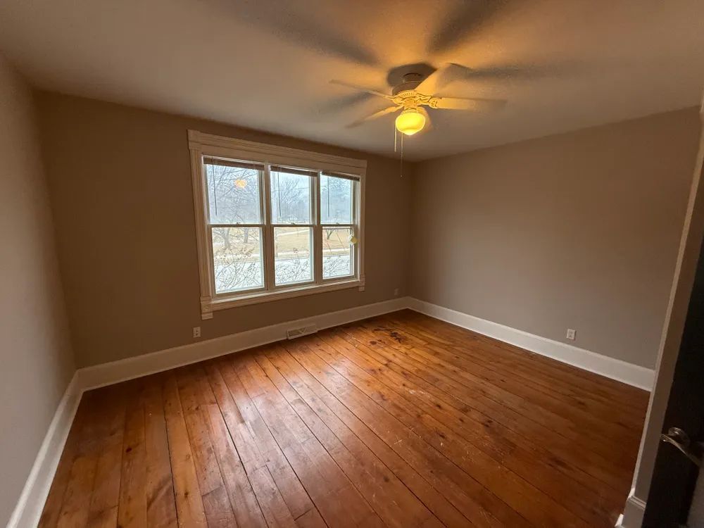 An empty room with hardwood floors and a ceiling fan.
