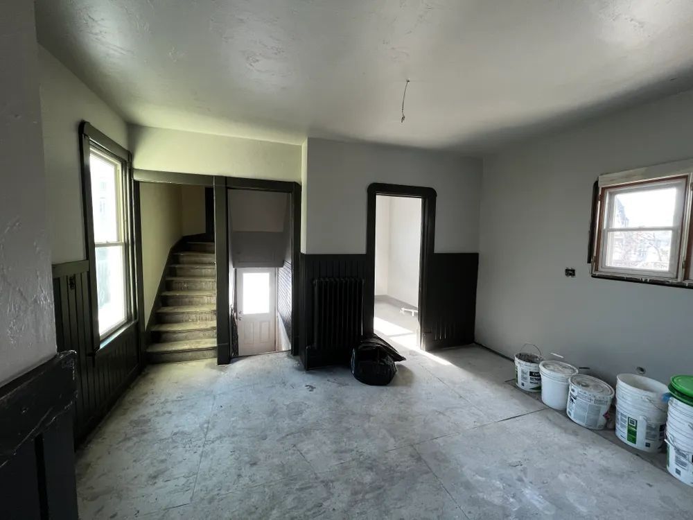An empty room with buckets of paint on the floor and stairs.