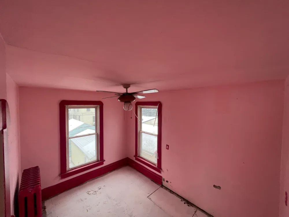 A room with pink walls and red trim and a ceiling fan