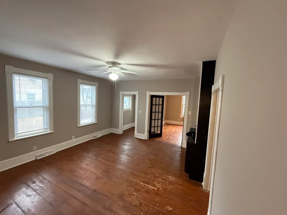 An empty living room with hardwood floors and a ceiling fan.