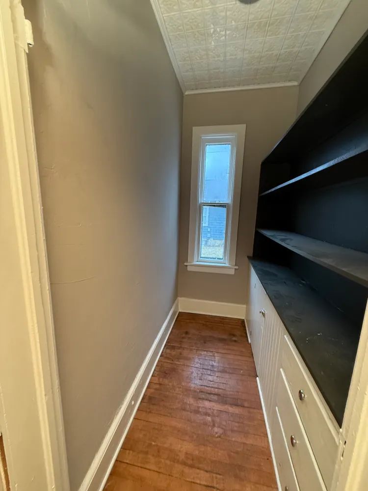 A long hallway with a window and shelves in a house.