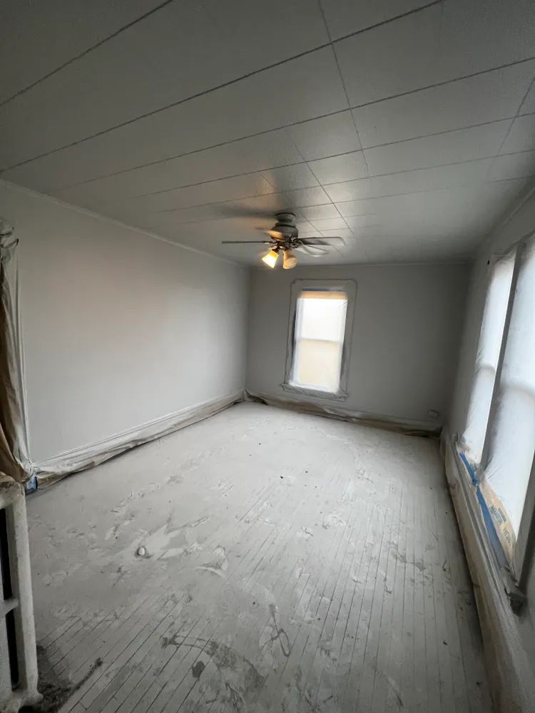 An empty room with a ceiling fan and a window.