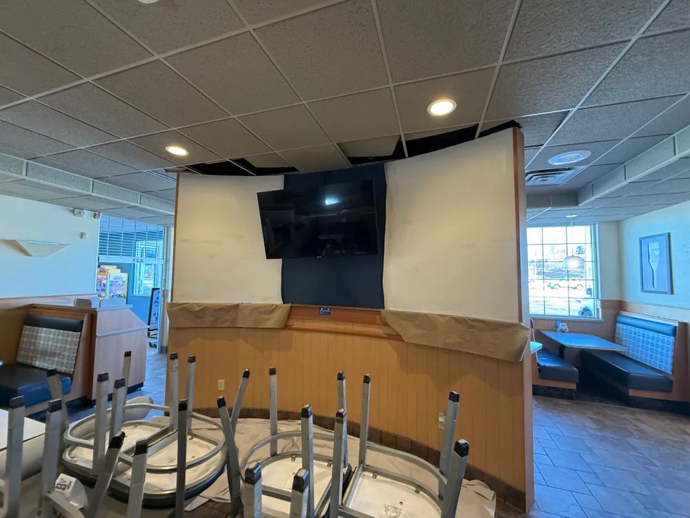 A restaurant with tables and chairs stacked on top of each other and a flat screen tv on the wall.