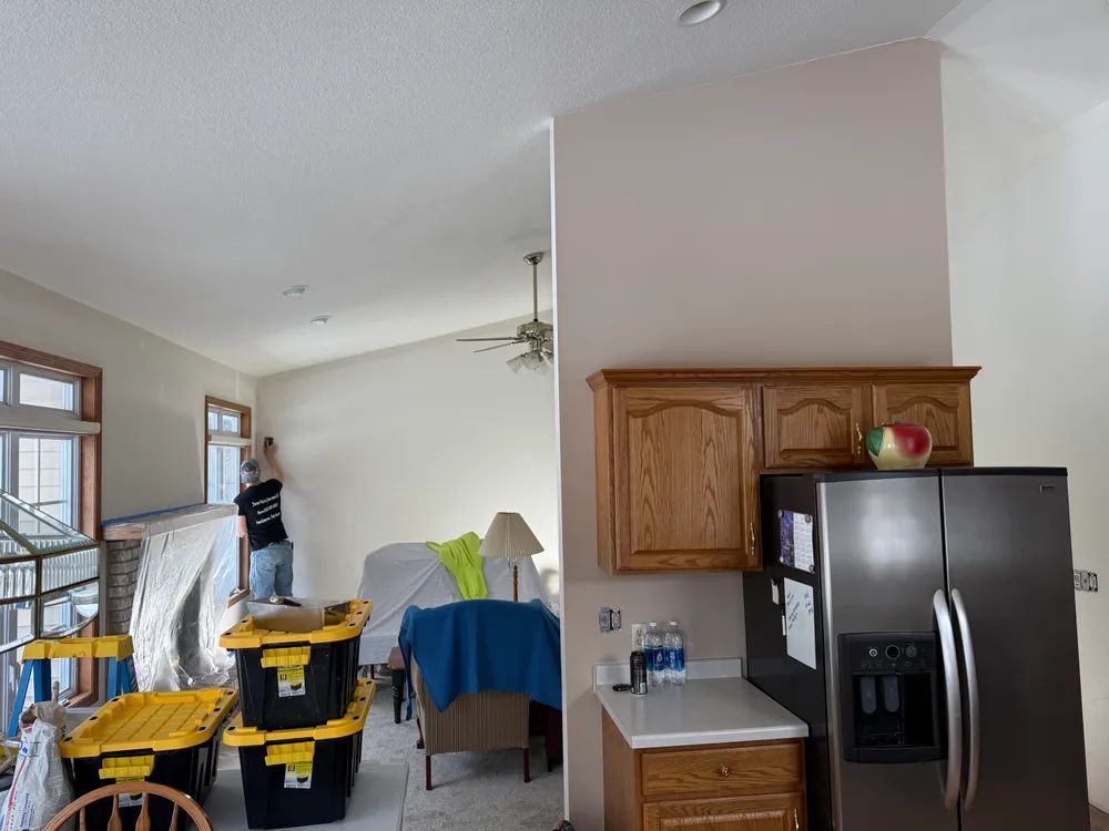 A man is painting a wall in a living room and a kitchen.