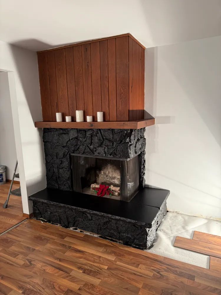 A fireplace with a wooden mantle and candles on it in a living room.