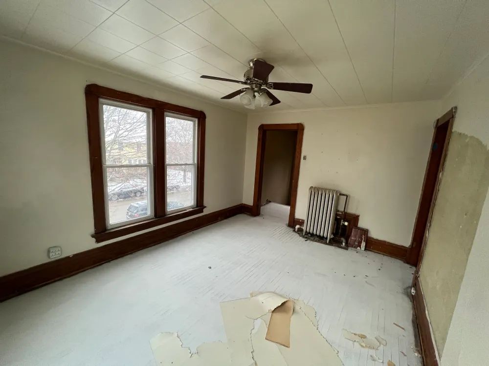 An empty room with a ceiling fan and two windows.