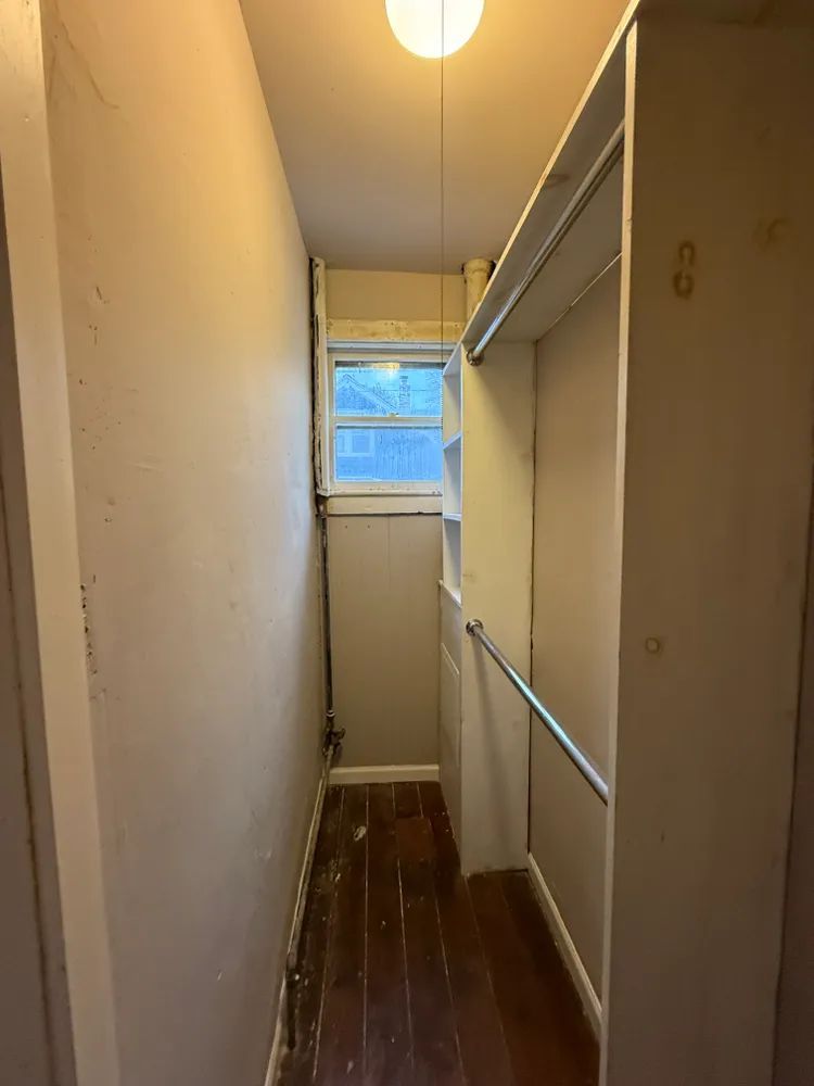 A walk in closet with hardwood floors and a window.