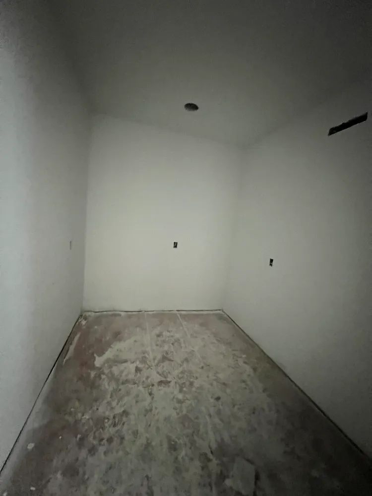 An empty room with white walls and a brown floor.