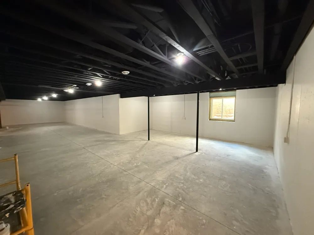 An empty basement with a window and a black ceiling.