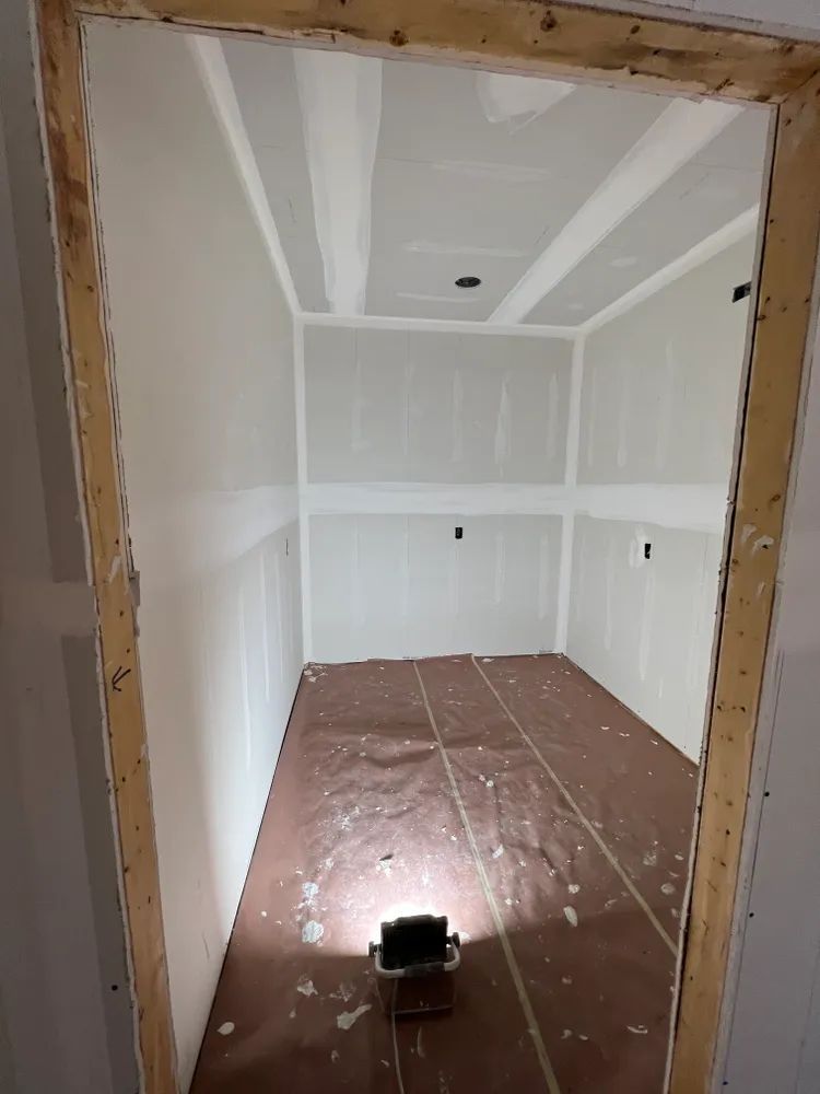 A room with white walls and a brown floor is being painted.