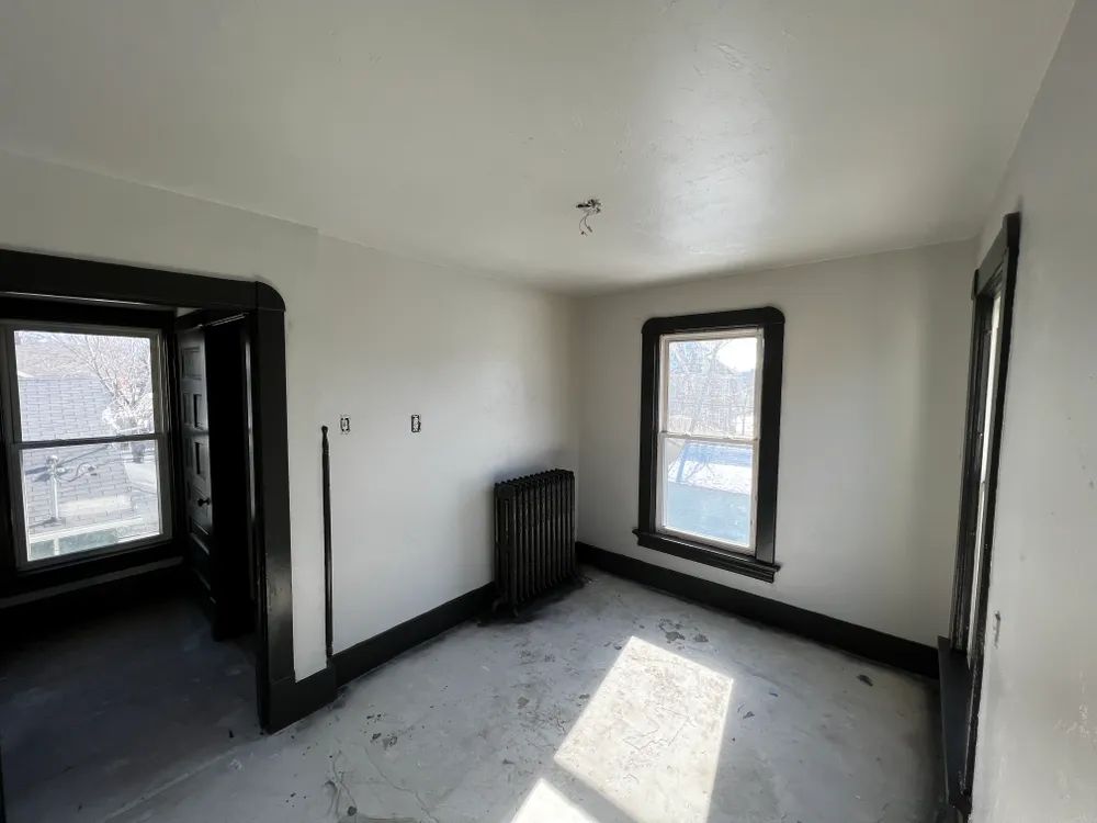 An empty room with a radiator and two windows
