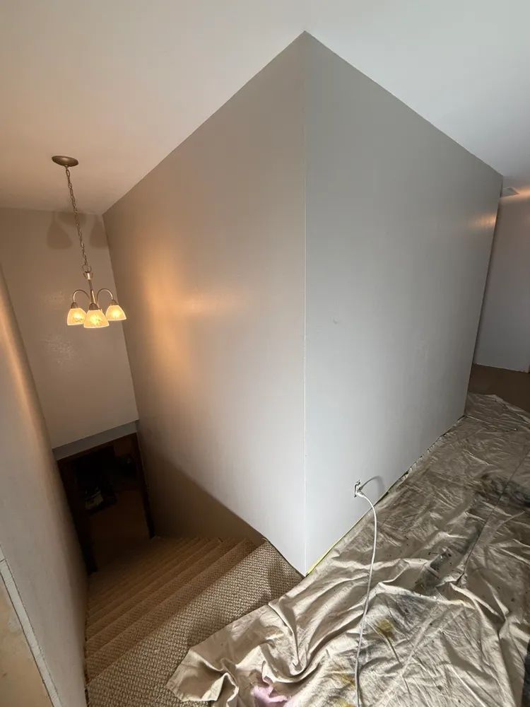 A room with a corner that is being painted and a chandelier hanging from the ceiling.