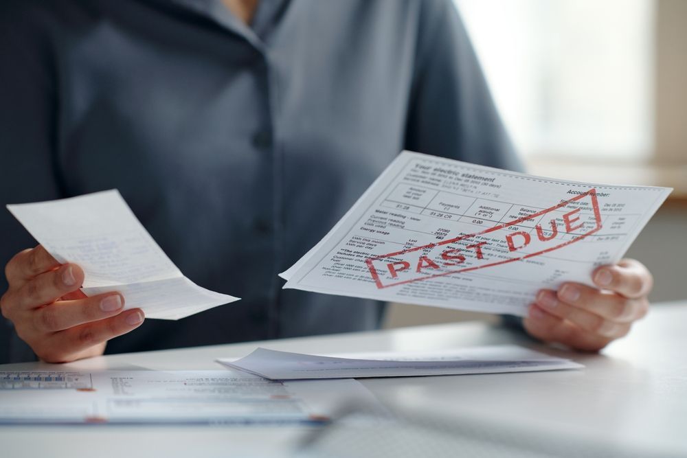 Person holding bills and an invoice stamped “PAST DUE” at a desk