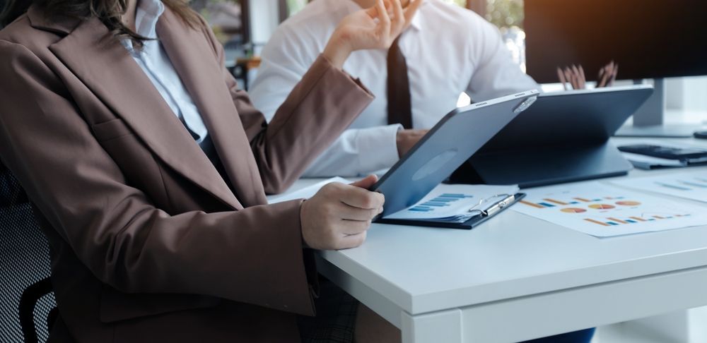 Two coworkers discussing charts at a desk with a laptop and papers