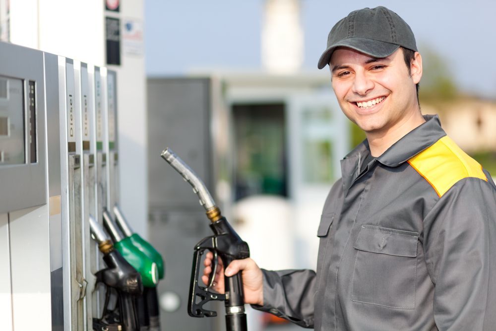 A man is smiling while pumping gas at a gas station