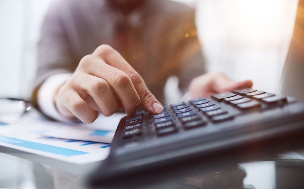 A person using a calculator, with charts and papers on the table.