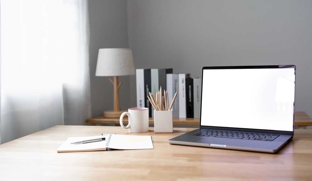 A laptop computer with a white screen is sitting on a wooden desk.