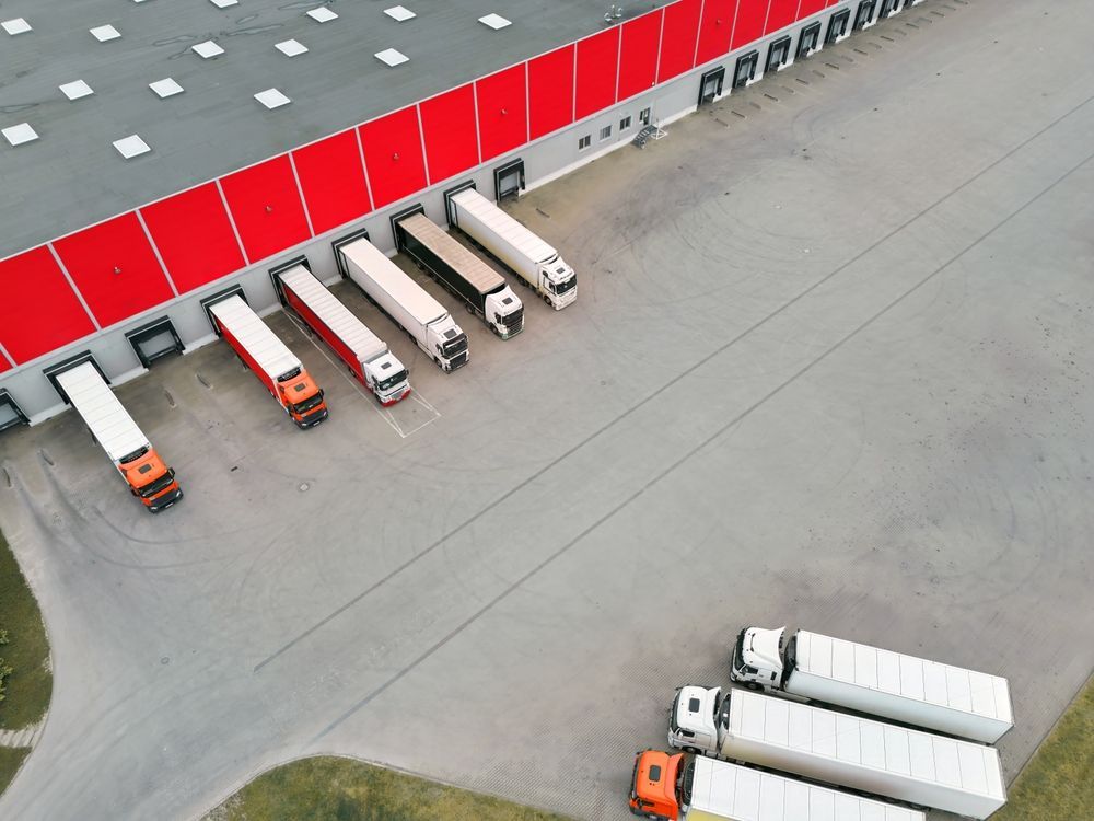 Trucks loading/unloading at a red and gray warehouse dock. Several trucks are docked, with others nearby.