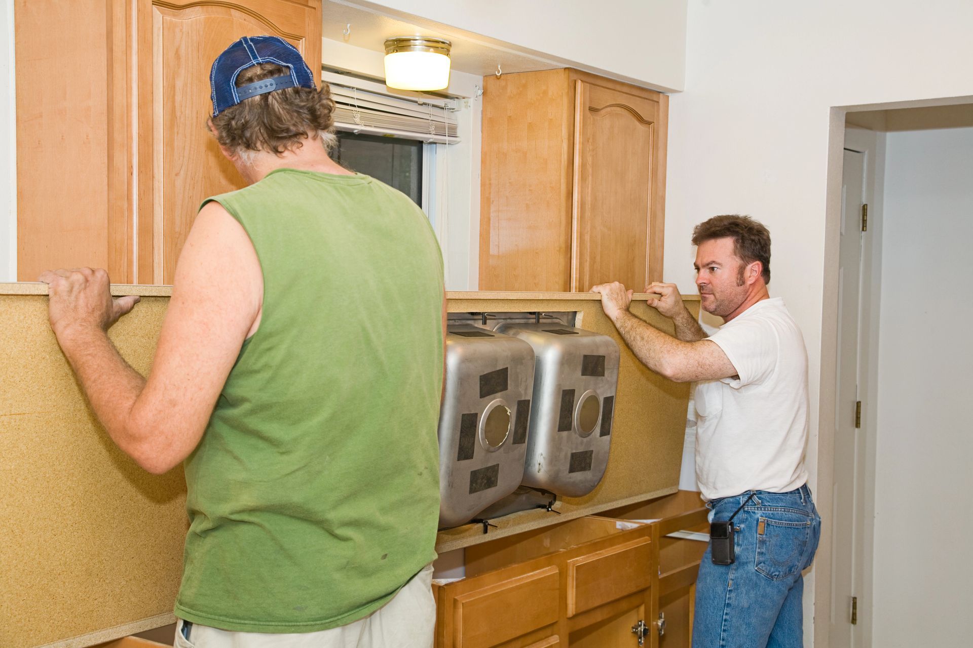 Two carpenters installing a wooden cabinet unit in a kitchen.