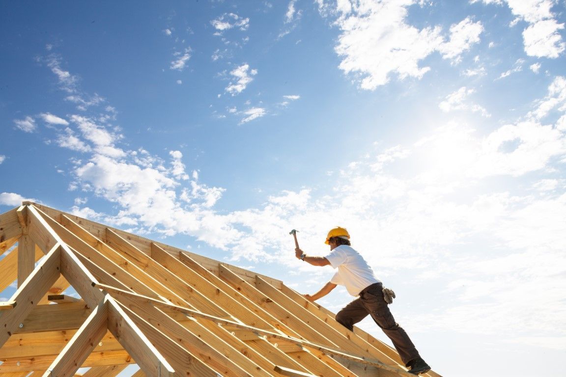 Roofer hammering wood beams against a bright blue sky.