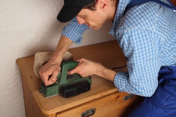 Woodworker using a power sander on a custom wooden cabinet.