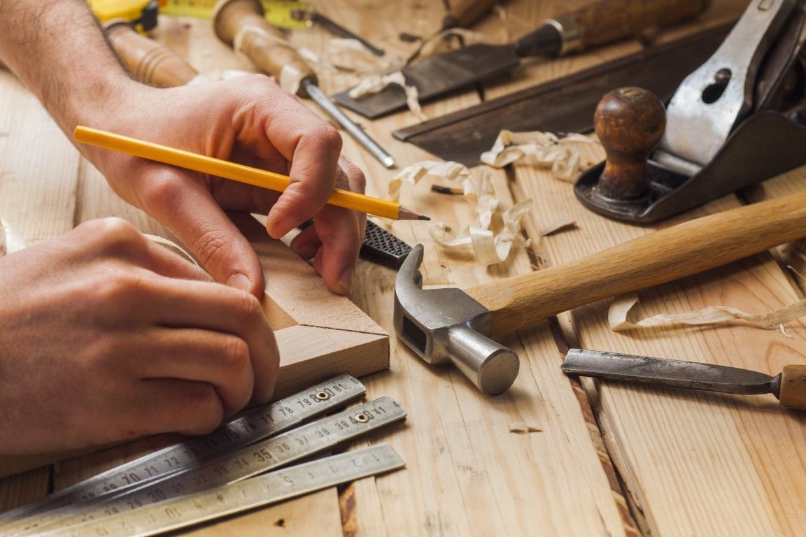Close-up of a carpenter’s hands measuring wood with a pencil.