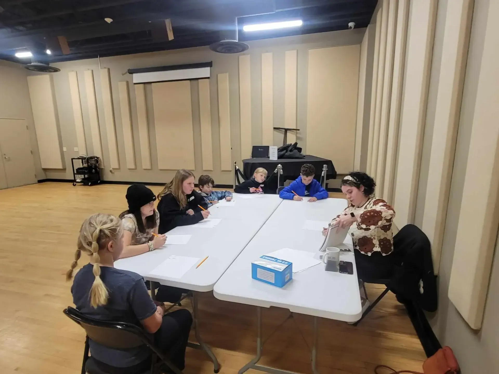 Group of people seated around tables in a room, some looking at papers.