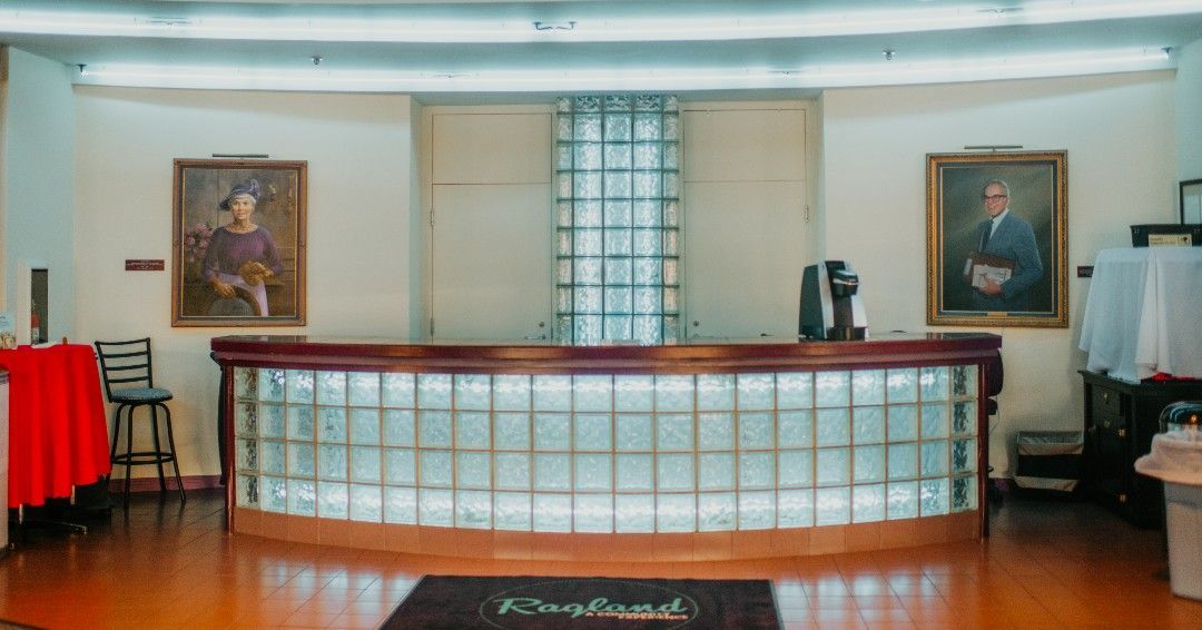 Reception area with curved glass block counter, portraits, and wooden floor.