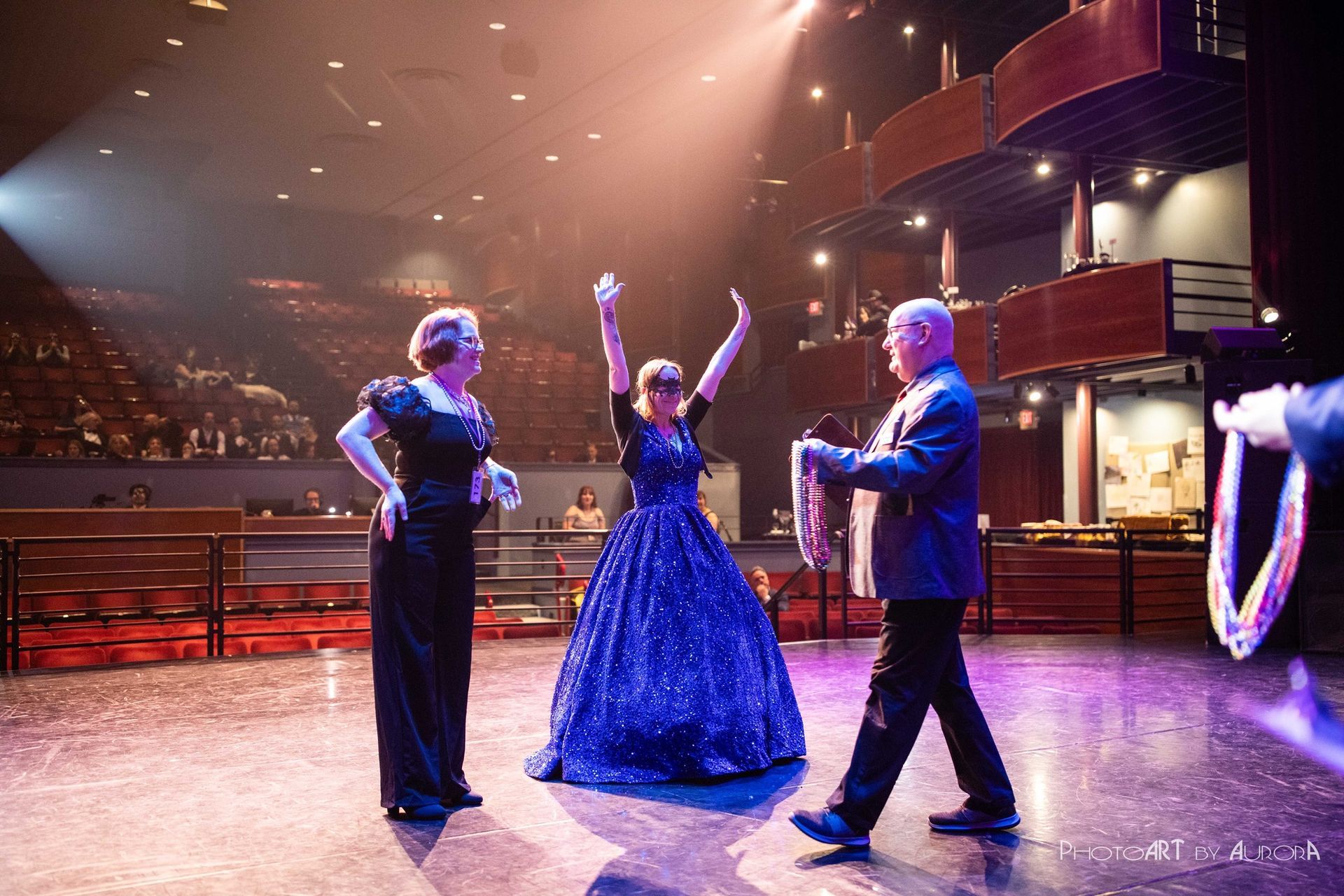 Magician on stage with two assistants; one holding rings, another with arms raised. Dramatic lighting.