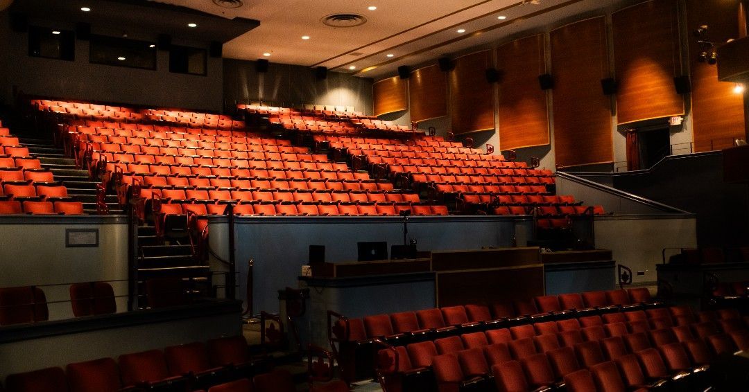 Empty auditorium with rows of red seats, stage, and dim lighting.