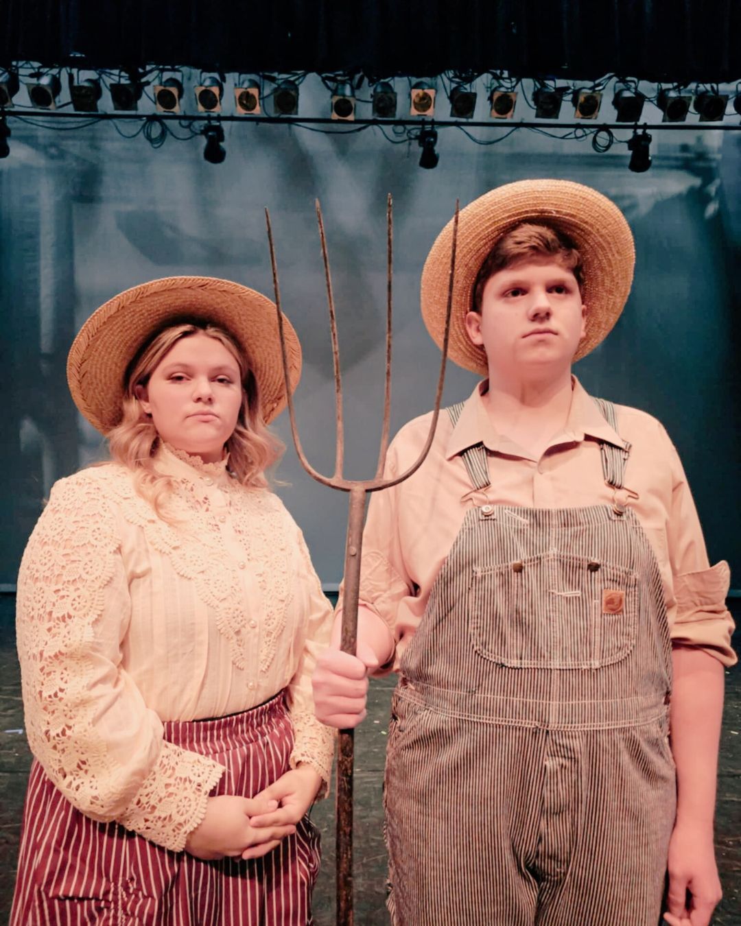 People stand in a line on a theater stage, facing the audience. Stage lights are above.