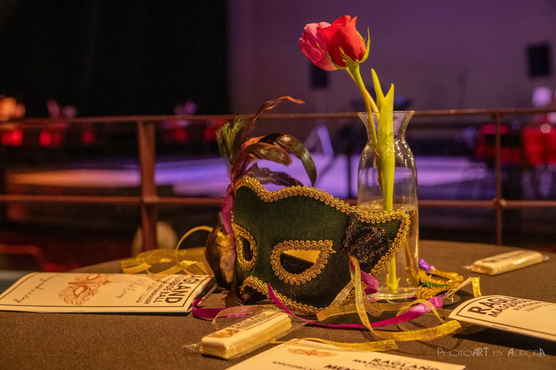 Mardi Gras table setting with mask, rose in a vase, cards, and purple and gold decorations.