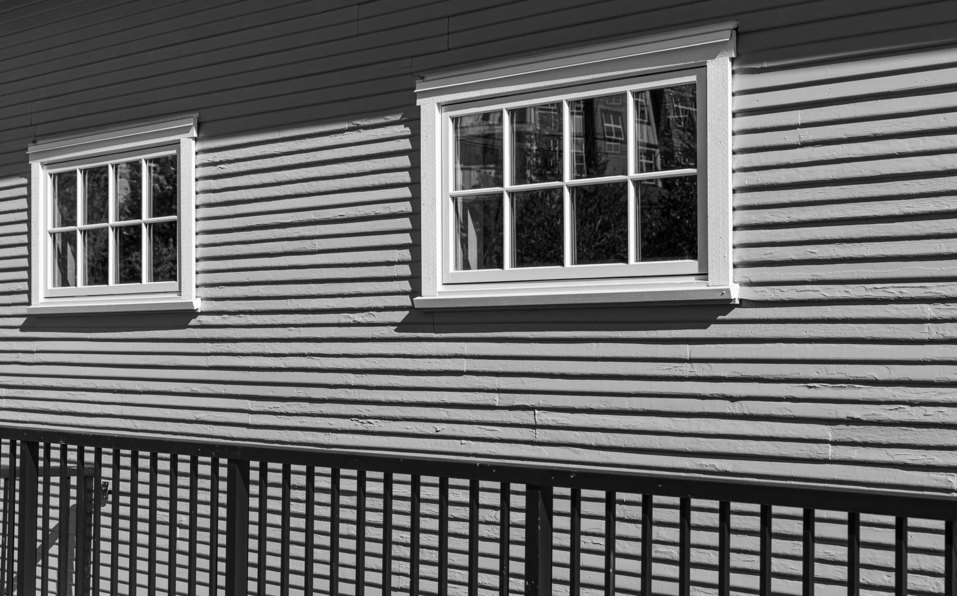 Two vintage identical single hung windows on a gray colour exterior wall. The windows with white trim