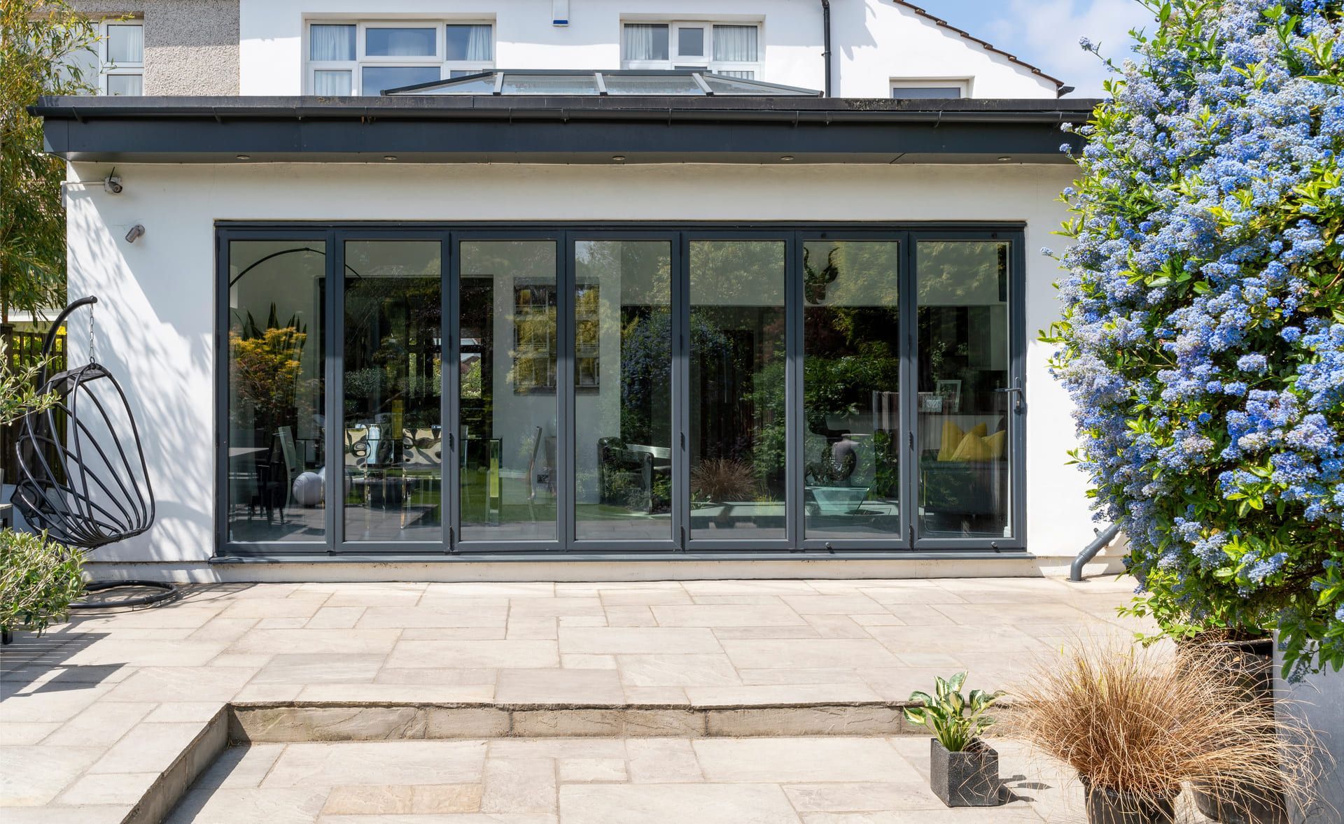 Stylish, closed, bifold doors with plants in spring, summer, revealing interior of a designer, lifestyle, kitchen diner room and indian sandstone patio