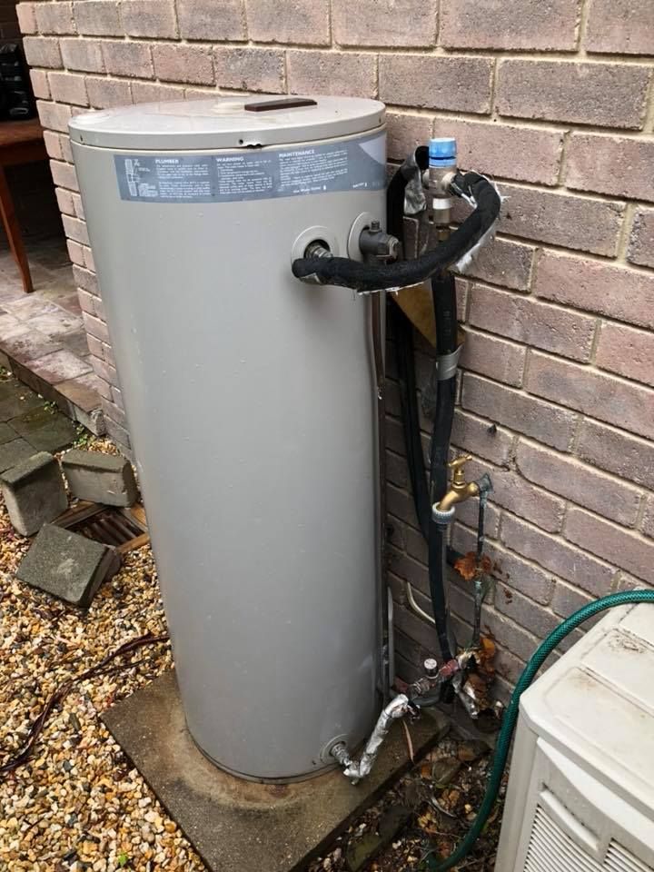 A cylindrical water heater against a brick wall; pipes and connections are visible. — Precise Plumbing & Drainage in Gungahlin, ACT