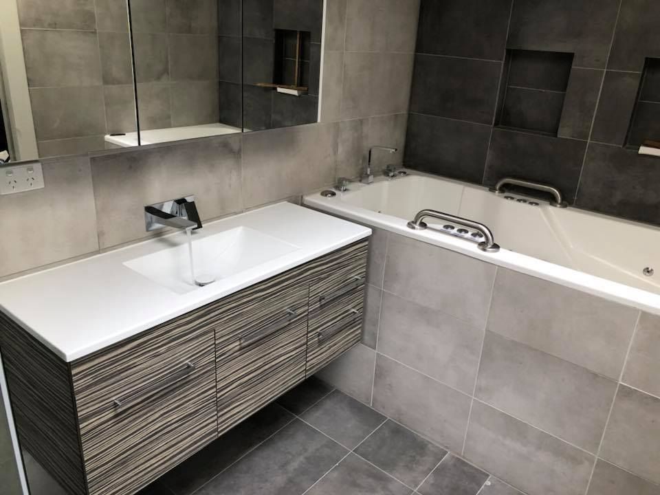 Modern bathroom with grey tile, white vanity, built-in tub, and silver fixtures. — Precise Plumbing & Drainage In Conder, ACT