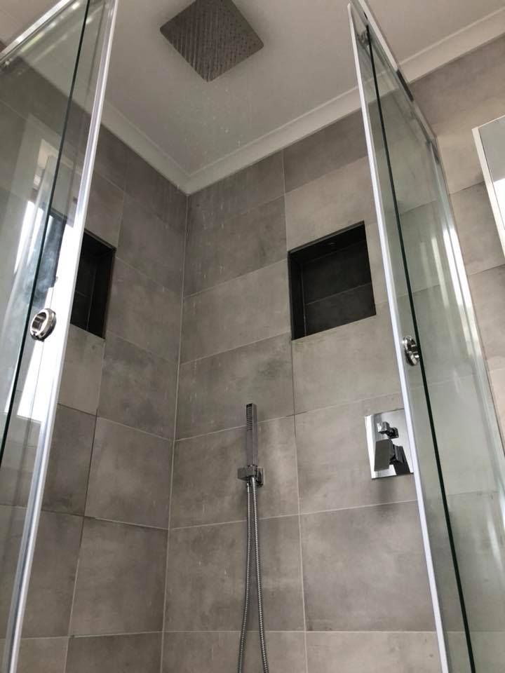 A modern shower with grey tiled walls, glass doors, and a rain showerhead. — Precise Plumbing & Drainage in Belconnen, ACT