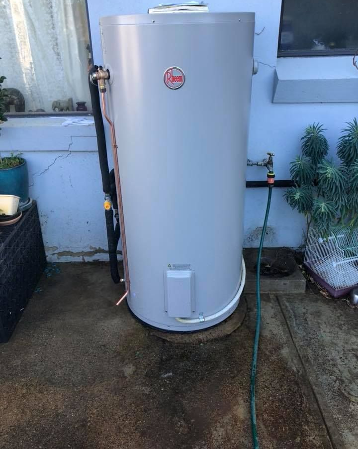 Grey Rheem hot water heater outside near a water tap and small plants. — Precise Plumbing & Drainage In Conder, ACT