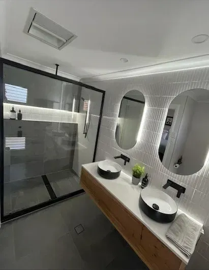 Modern bathroom with a shower, vanity with two sinks, and oval mirrors with LED lighting. — Precise Plumbing & Drainage in Gungahlin, ACT