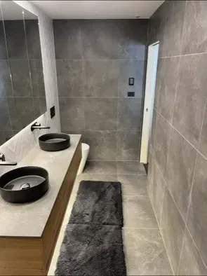 Modern bathroom with dark grey tile, two black sinks, and a grey rug. — Precise Plumbing & Drainage in Tuggeranong, ACT