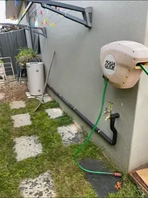 A Hose Reel on A Grey Wall with Green Hose, Adjacent Water Tap, and Pathway — Precise Plumbing & Drainage in Belconnen, ACT