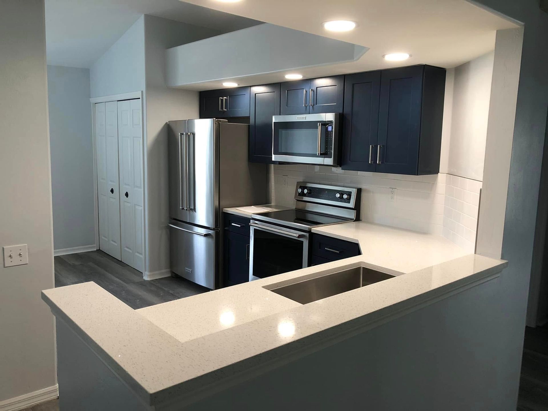 Modern kitchen with dark cabinets, stainless appliances, and a light quartz breakfast bar