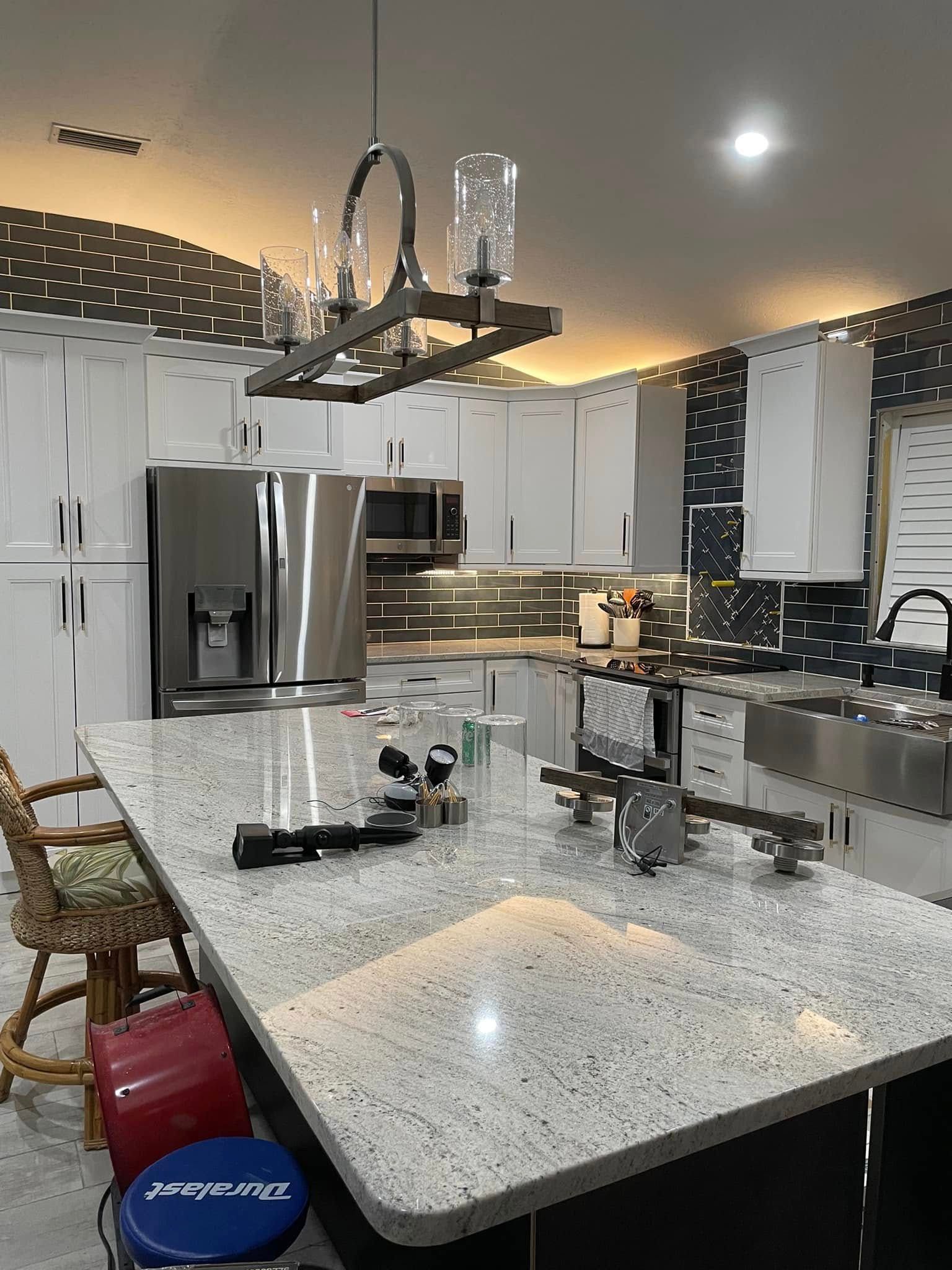 Modern kitchen with white cabinets, stainless appliances, and a large granite island under pendant lights