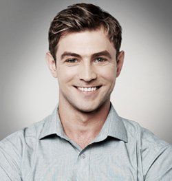 A man in a blue shirt is smiling with his arms crossed