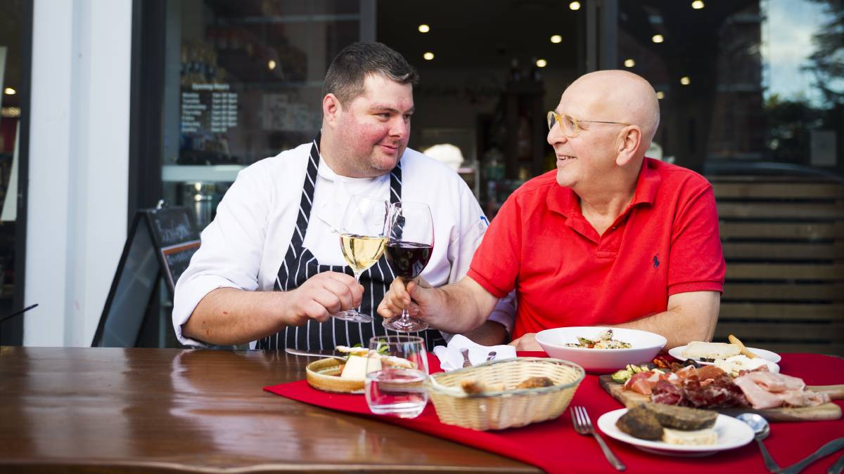 Two men are sitting at a table eating food and drinking wine.