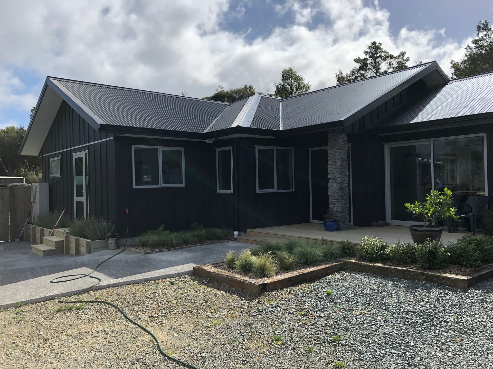 Black house with a dark roof and gravel driveway under a cloudy sky.