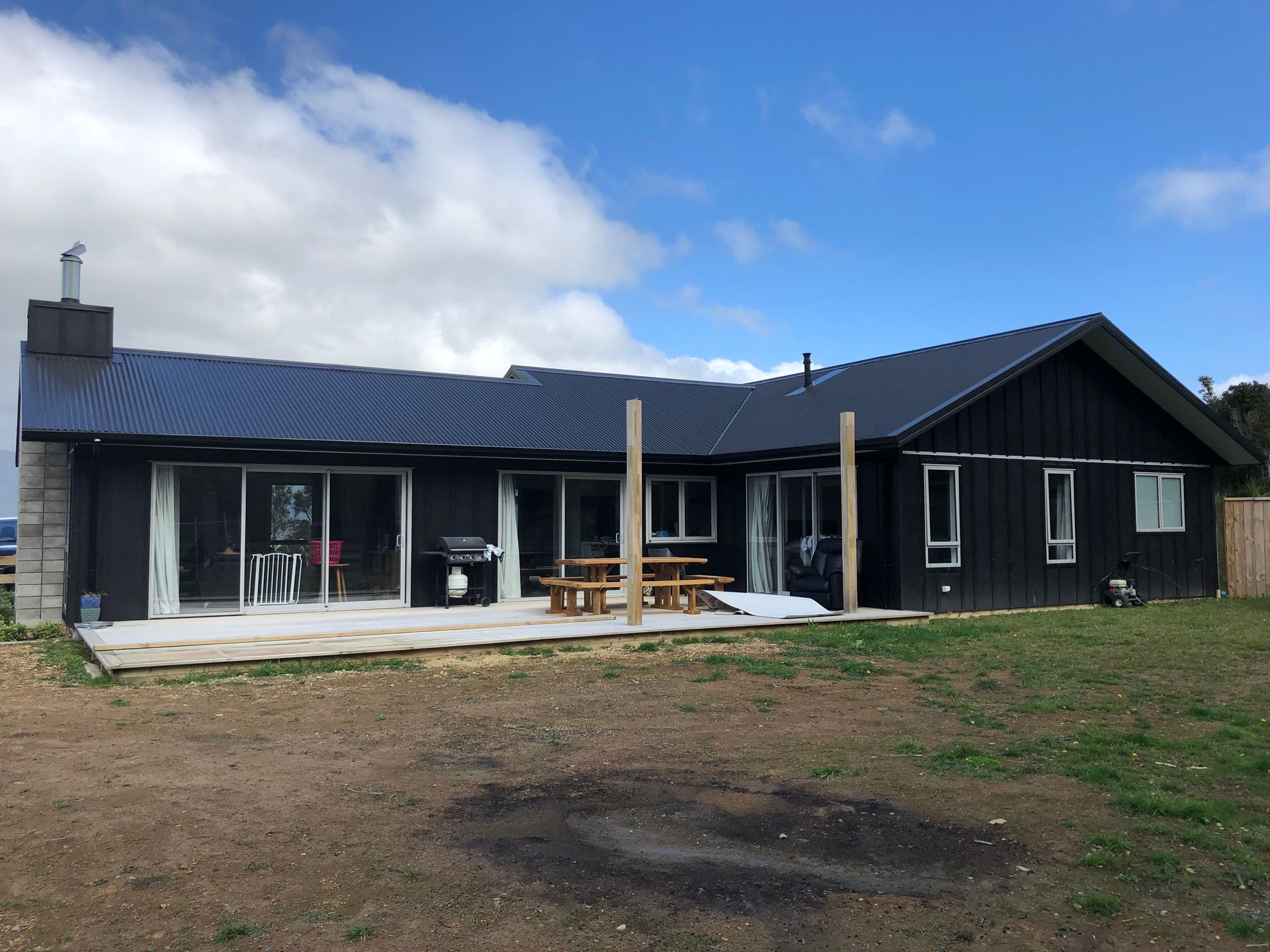 Black house with a dark roof and a wooden deck on a sunny day.