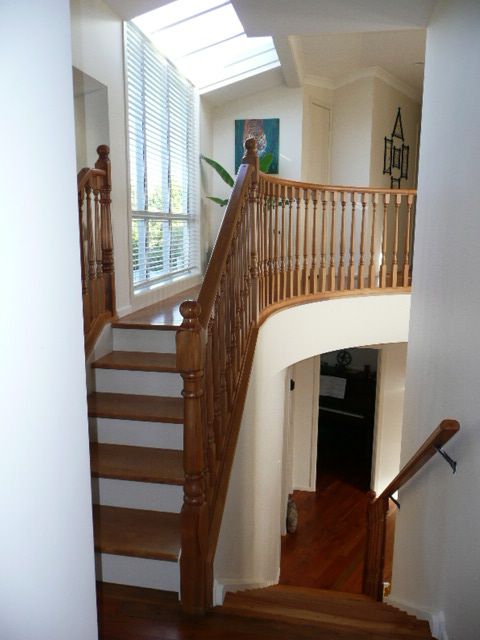 Wooden staircase with curved railing in a home, leading to a second floor with a window and skylight.