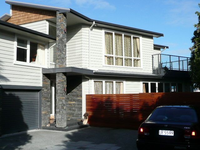 Two-story house with light siding and a stone column entrance. A car is parked in the driveway.