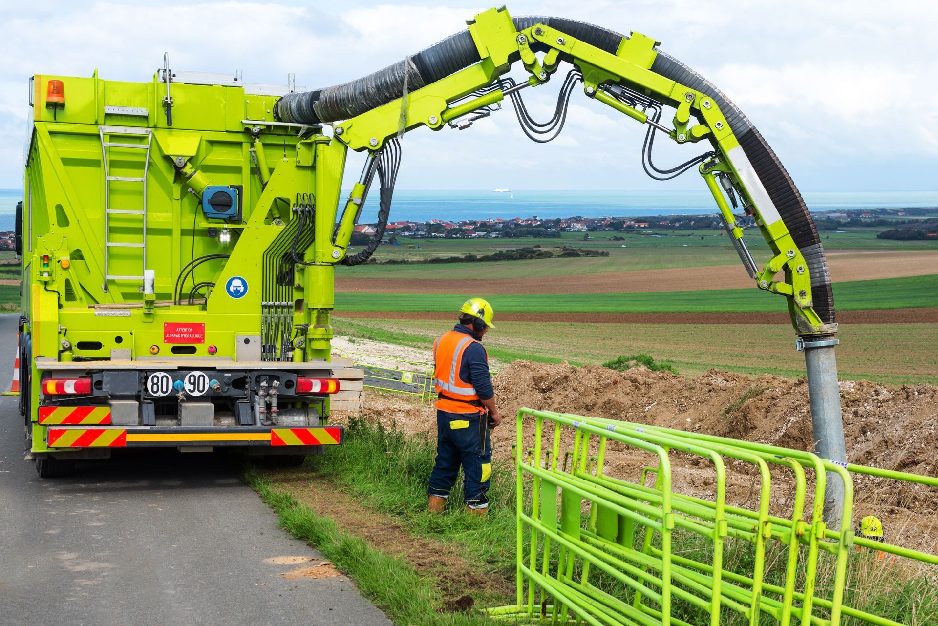 Industrial vacuum excavation truck with boom arm deployed at an outdoor excavation site with worker in high-visibility safety gear